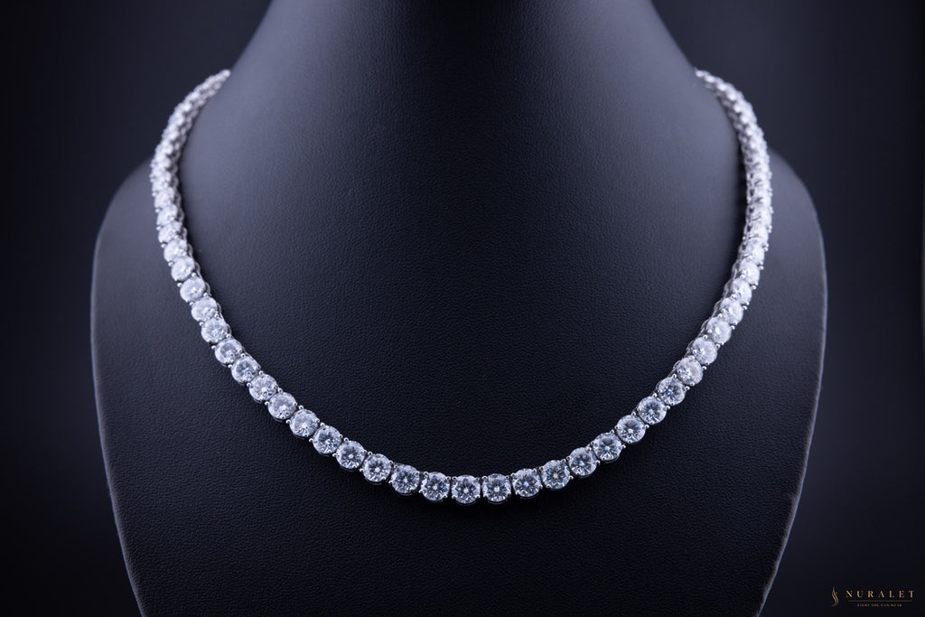 A sparkling diamond tennis necklace displayed on a black jewelry bust against a dark background.